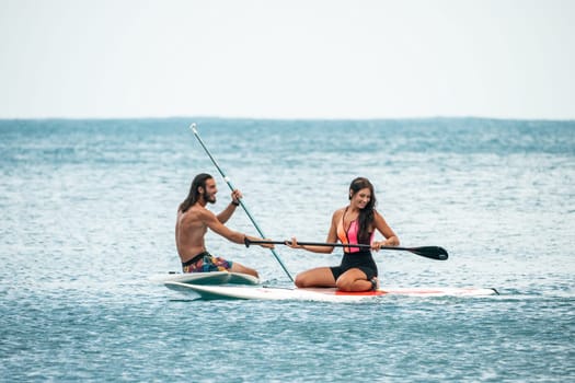 Sea woman and man on sup. Silhouette of happy young woman and man, surfing on SUP board, confident paddling through water surface. Idyllic sunset. Active lifestyle at sea or river