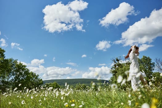 a happy woman in a light dress runs through a chamomile field against a clear sky. High quality photo