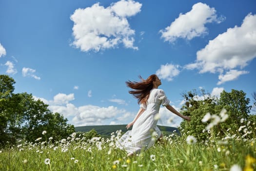 a happy woman in a light dress runs through a chamomile field against a clear sky. High quality photo