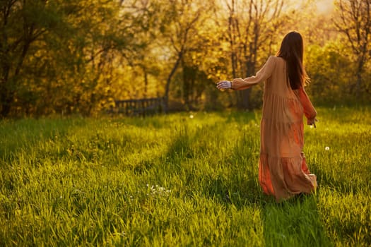 a slender woman with long hair walks in a field posing with her back to the camera, illuminated by the rays of the setting sun. High quality photo