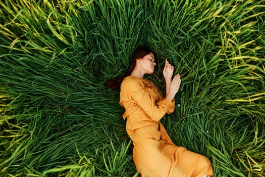 a relaxed woman enjoys summer lying in the tall green grass with her eyes closed. Photo taken from above. High quality photo