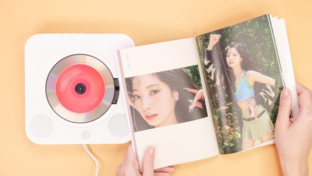 Hands holding Twice Between 1 and 2 mini Album photobook on yellow. Music CD player. South Korean girl group Twice. Space for text. Gatineau, QC Canada - December 27 2022