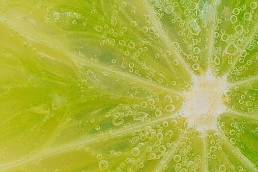 Slice of ripe lime in water. Close-up of lime in liquid with bubbles. Slice of ripe lime in sparkling water. Macro horizontal image of fruit in carbonated water