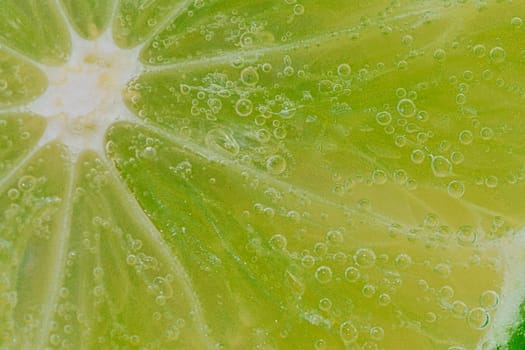 Close-up of a lime slice in liquid with bubbles. Slice of ripe lime in water. Close-up of fresh lime slice covered by bubbles. Macro horizontal image