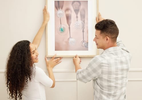 Lets make this house a home. Shot of a couple hanging art in their new home