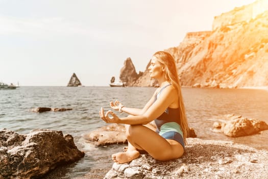 Yoga on the beach. A happy woman meditating in a yoga pose on the beach, surrounded by the ocean and rock mountains, promoting a healthy lifestyle outdoors in nature, and inspiring fitness concept