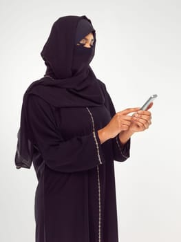 Muslim, phone and social media with an islamic woman in studio on a gray background for communication or networking. Contact, internet and islam with a female typing a text message or online post.