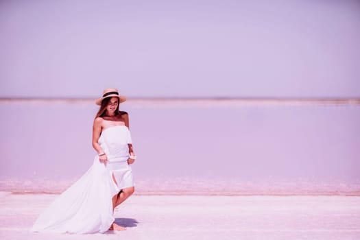 Woman in pink salt lake. She in a white dress and hat enjoys the scenic view of a pink salt lake as she walks along the white, salty shore, creating a lasting memory