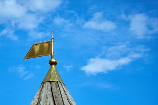 Bronze tip in the form of a flag on a pointed wooden roof against the sky