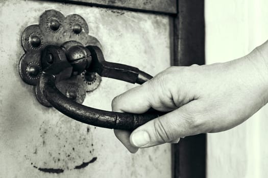 A hand opens an ancient door. Door handle in the form of a ring. Black and white toned image