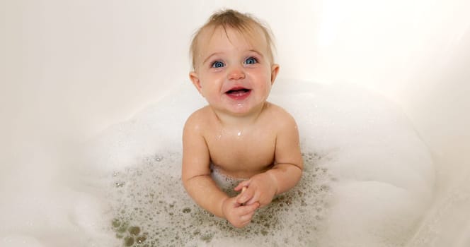 Happy baby girl laughing and splashing in bath tub