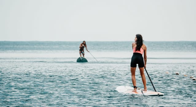 Sea woman and man on sup. Silhouette of happy young woman and man, surfing on SUP board, confident paddling through water surface. Idyllic sunset. Active lifestyle at sea or river