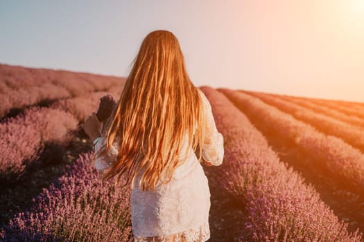 Close up portrait of young beautiful woman in a white dress and a hat is walking in the lavender field and smelling lavender bouquet.