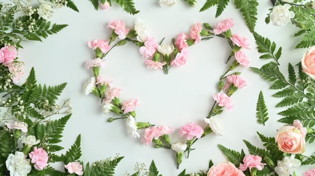 Heart shape made of pink rose, carnation and fern leaves on white background. Flat lay, top view.