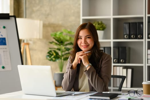 Image of successful startup business founder sitting in modern office and smiling at camera.