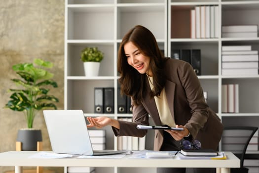 Cheerful female entrepreneur in trendy suit having video call in laptop at modern office.