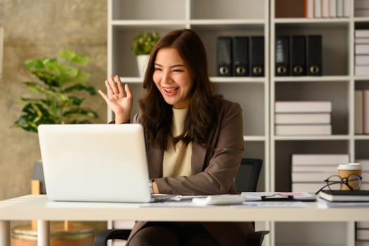 Cheerful female entrepreneur consulting client online, discussing working issues remotely via laptop at workplace.