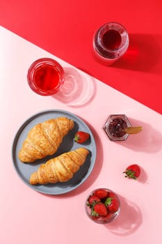 Delicious breakfast with fresh puff croissants, berry juice, jam and fresh berries on a pink and red background.