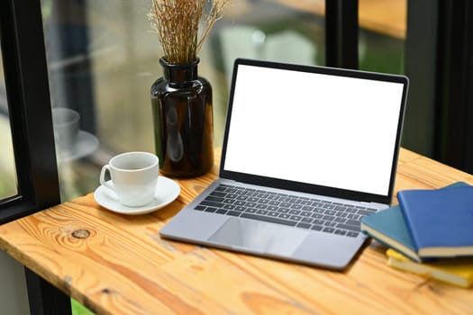 Comfortable workplace with laptop, cup of coffee and books on wooden table.