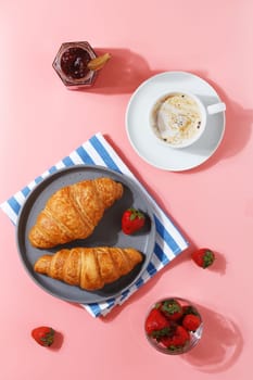 Delicious breakfast with fresh croissants, coffee, berry jam and fresh berries on a pink background.