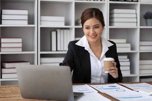 Young woman enjoying her coffee while working or studying on laptop computer at office.