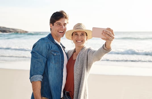 Young couple, beach selfie and smile in summer sunshine for love, romance or happy for social media post. Man, woman and profile picture for blog, app or internet by ocean, waves or sea for vacation.