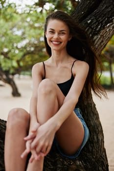 sitting woman smiling looking vacation outdoors sea lifestyle nature tree relax summer fool sunny trunk paradise bikini sky ocean beautiful relaxation