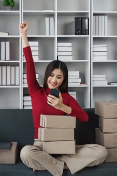 Young Women happy after new order from customer, business owner working at home office packaging on background. online shopping SME entrepreneur or freelance working concept.