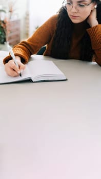 Woman writing in copybook. Business woman or young female student holding pen in hand writing in paper notebook journal, taking notes studying, doing homework, making checklist. Close up view.