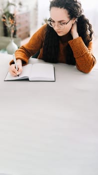 Woman writing in copybook. Business woman or young female student holding pen in hand writing in paper notebook journal, taking notes studying, doing homework, making checklist. Close up view.