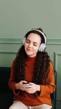 A calm, relaxed, carefree young woman listens to music, an audio podcast or audiobook on her cell phone while sitting at home, meditating and relaxing, feeling peace of mind with her eyes closed