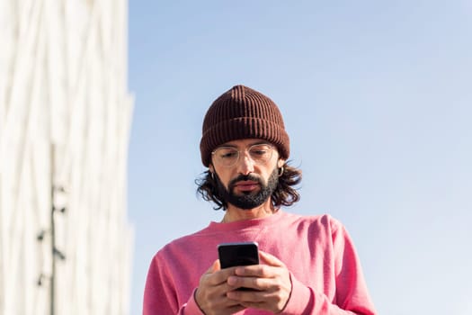 stylish bearded young man in pink jersey texting on his smart phone, concept of modern lifestyle and technology of communication, copy space for text