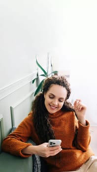 Happy lady browsing e-commerce sites or watching funny videos on a smartphone. Enjoying online leisure A smiling young woman uses a cell phone for online shopping or entertainment at home on the couch