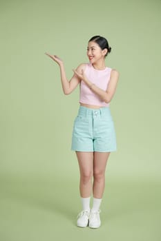 Young asian woman over isolated green background extending hands to the side for inviting to come