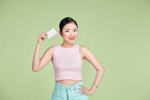 Beautiful young woman holding blank credit card against green background
