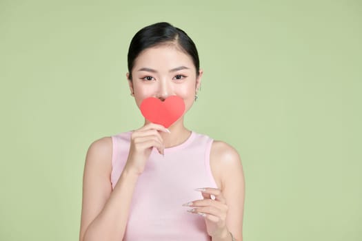 Playful Asian woman holding paper heart in front of her mouth.