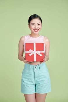 Happy pretty young woman holding gift box over green background