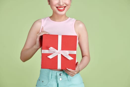 Happy pretty young woman holding gift box over green background