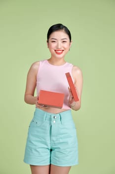 Portrait of beautiful young woman posing, opening present box over green background