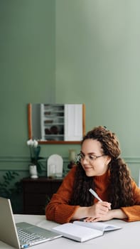 Remote Learning and Working: Young Female Student Studying Online with Laptop at Home Office. Effective Online Education: Young Female Student Learning and Writing Notes on Laptop at Home.