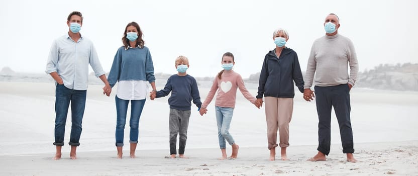 Covid, walking and family at the beach with face mask on, holding hands with grandparents, parents and children. Big family on a walk, stroll and relax by the ocean after covid 19 pandemic lockdown.