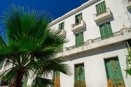 A low-rise deserted 1930s hotel with a decayed facade and green wooden window shutters under the summer blue sky.