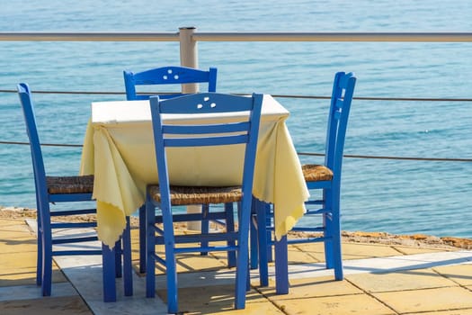 Empty tavern restaurant by the seafront with wooden chairs and tables under a bright sun in summer.
