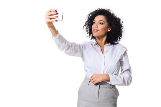 Beautiful brunette woman in classic white shirt and skirt make selfie on the phone. White background. Isolated
