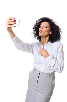 Beautiful brunette woman in classic white shirt and skirt make selfie on the phone. White background. Isolated