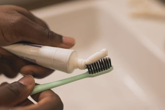 African american male hand holding toothbrush with toothpaste applied on it in bathroom. Close up of man hand ready for brushing teeth. Guy hand holding toothbrush with white tooth paste