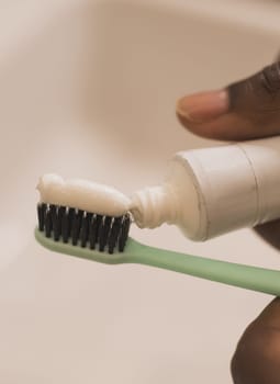 African american male hand holding toothbrush with toothpaste applied on it in bathroom. Close up of man hand ready for brushing teeth. Guy hand holding toothbrush with white tooth paste