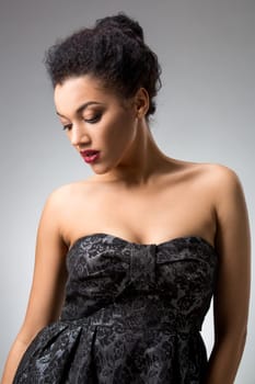 Portrait of beautiful brunette girl in the studio on a gray background in a black dress