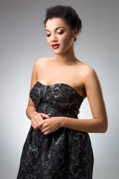 Portrait of beautiful brunette girl in the studio on a gray background in a black dress