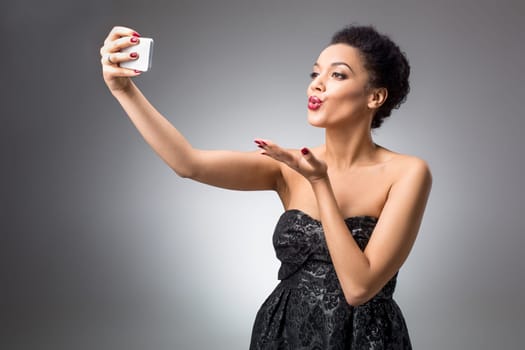 Portrait of a Beautiful brunette doing selfie in a black dress on a light background